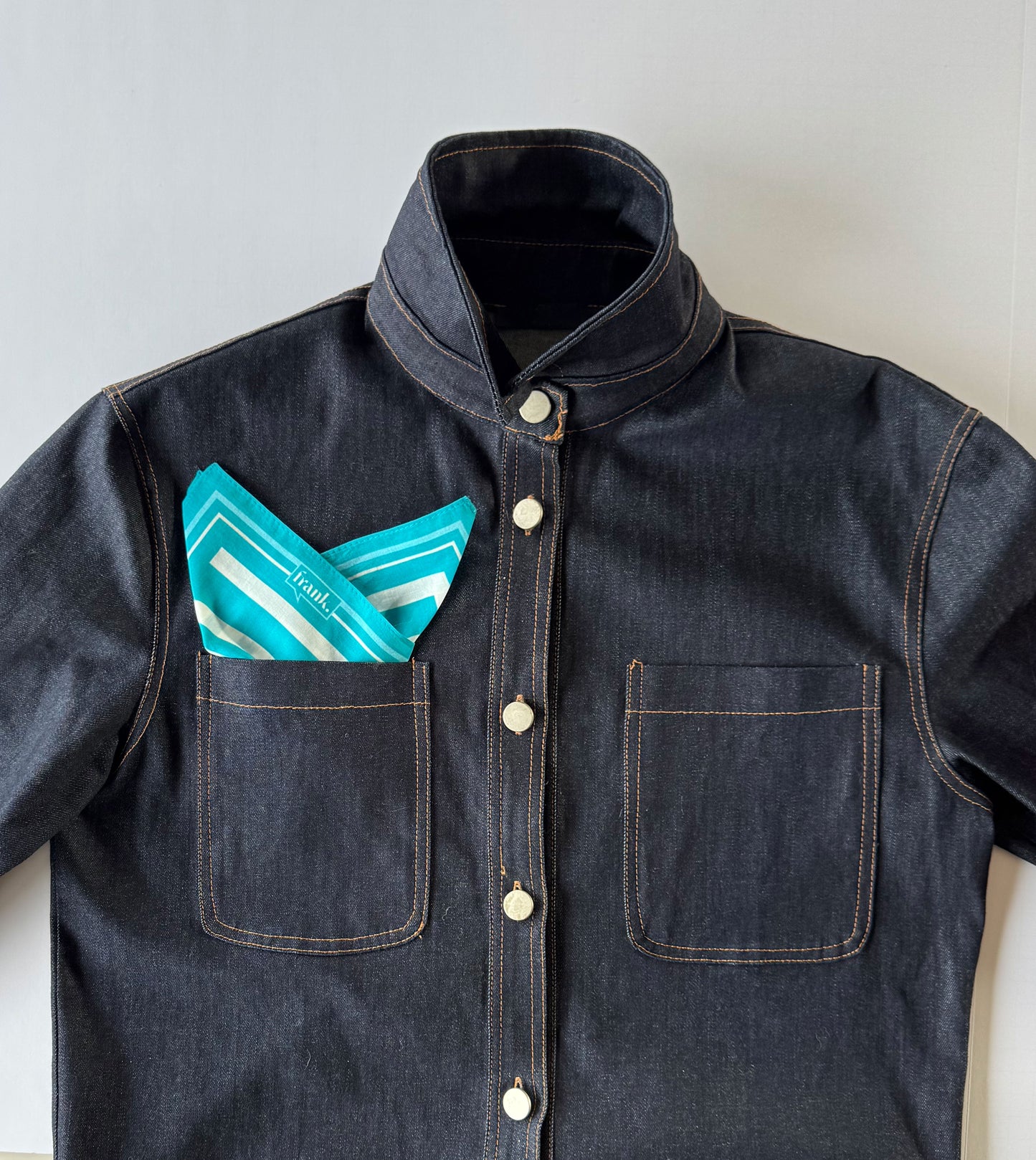 Dark denim shirt with a pocket containing a teal and white handkerchief on a light background