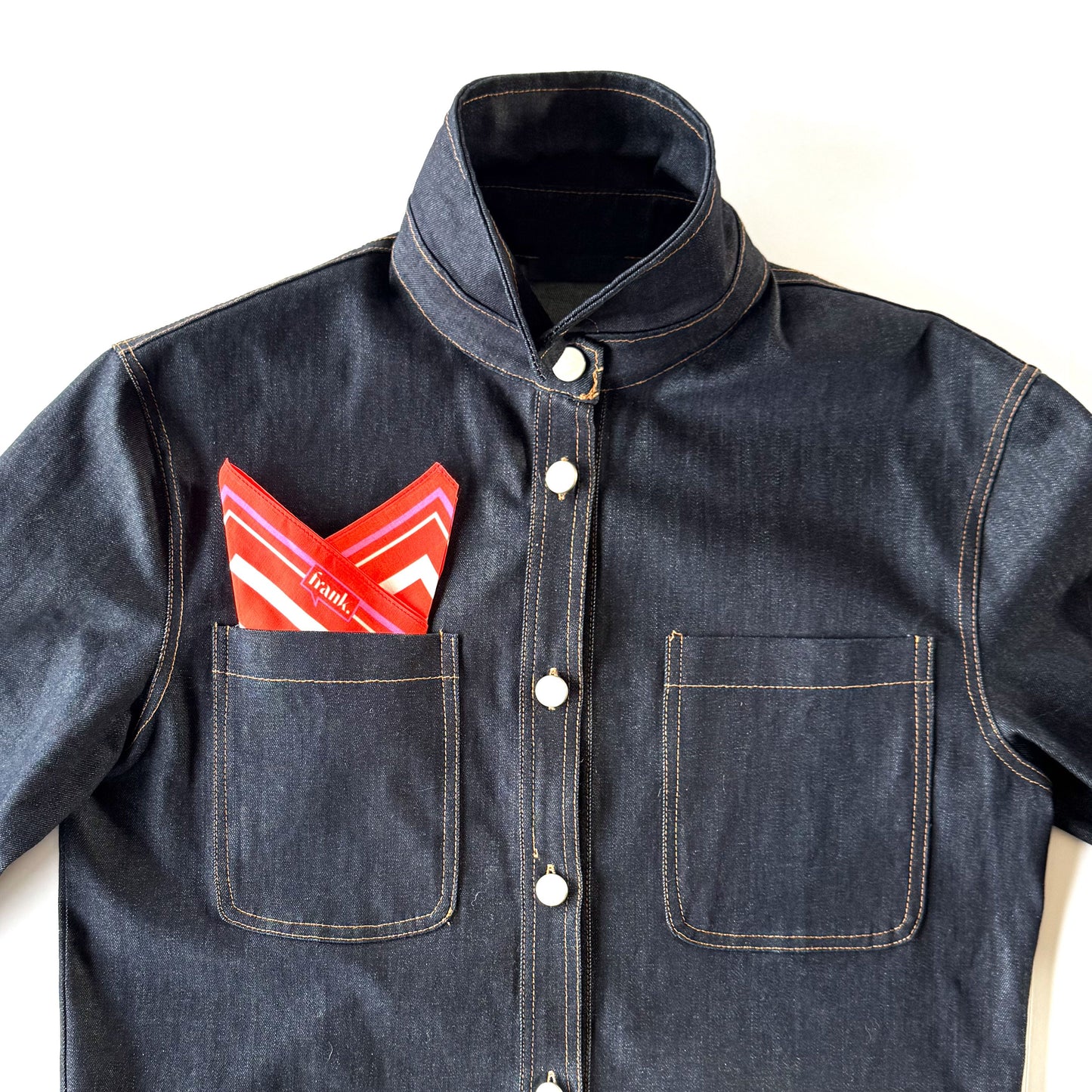 Denim jacket with a deep orange and white striped handkerchief in the pocket on a white background