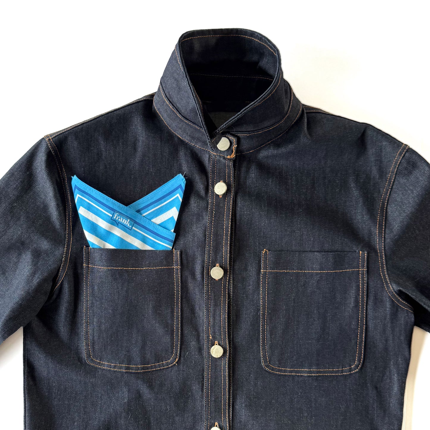 Denim jacket with a bright blue and white striped handkerchief in the pocket on a white background