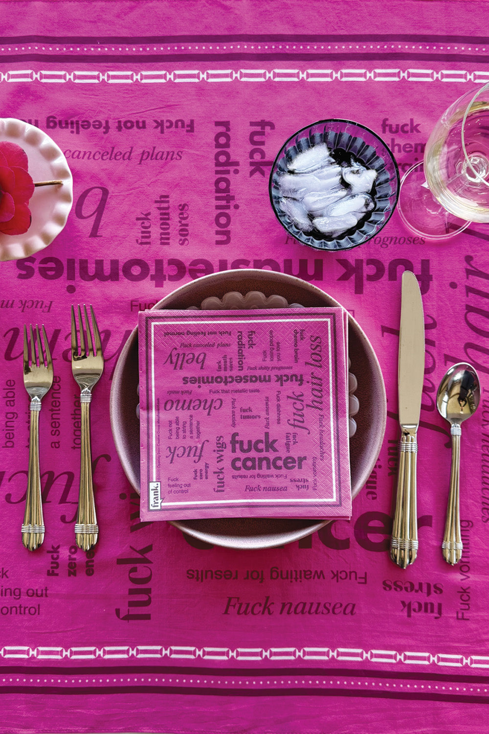 Hot pink and burgundy Fuck Cancer Cocktail napkin sitting on a plate on a tablescape of cancer words.