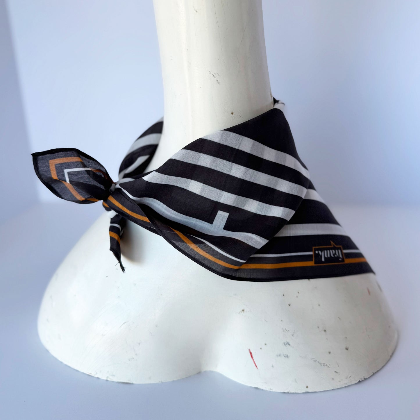 Black and white striped silk blend scarf with gold accents on a mannequin against a light gray background