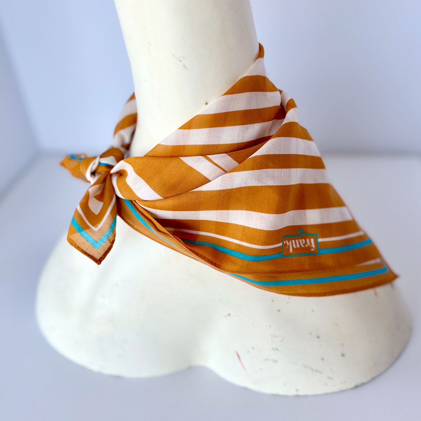 Mannequin wearing a gold striped scarf with a visible brand logo on a white background
