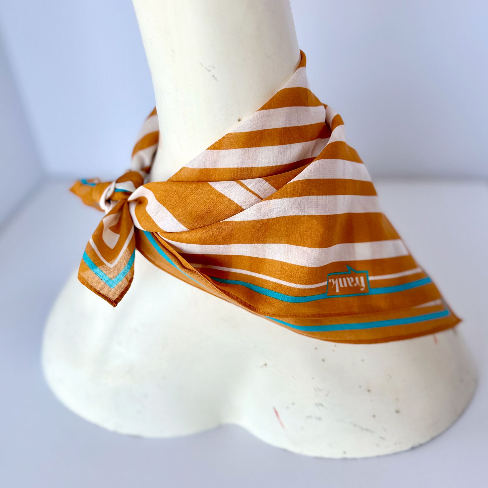 Mannequin wearing a gold striped scarf with a visible brand logo on a white background