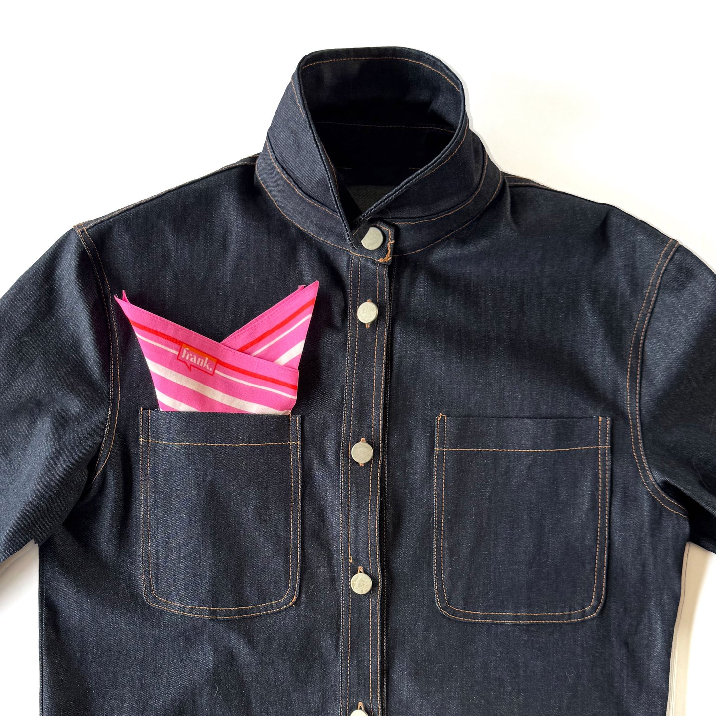 Denim jacket with a bright pink, orange and white striped handkerchief in the pocket on a white background