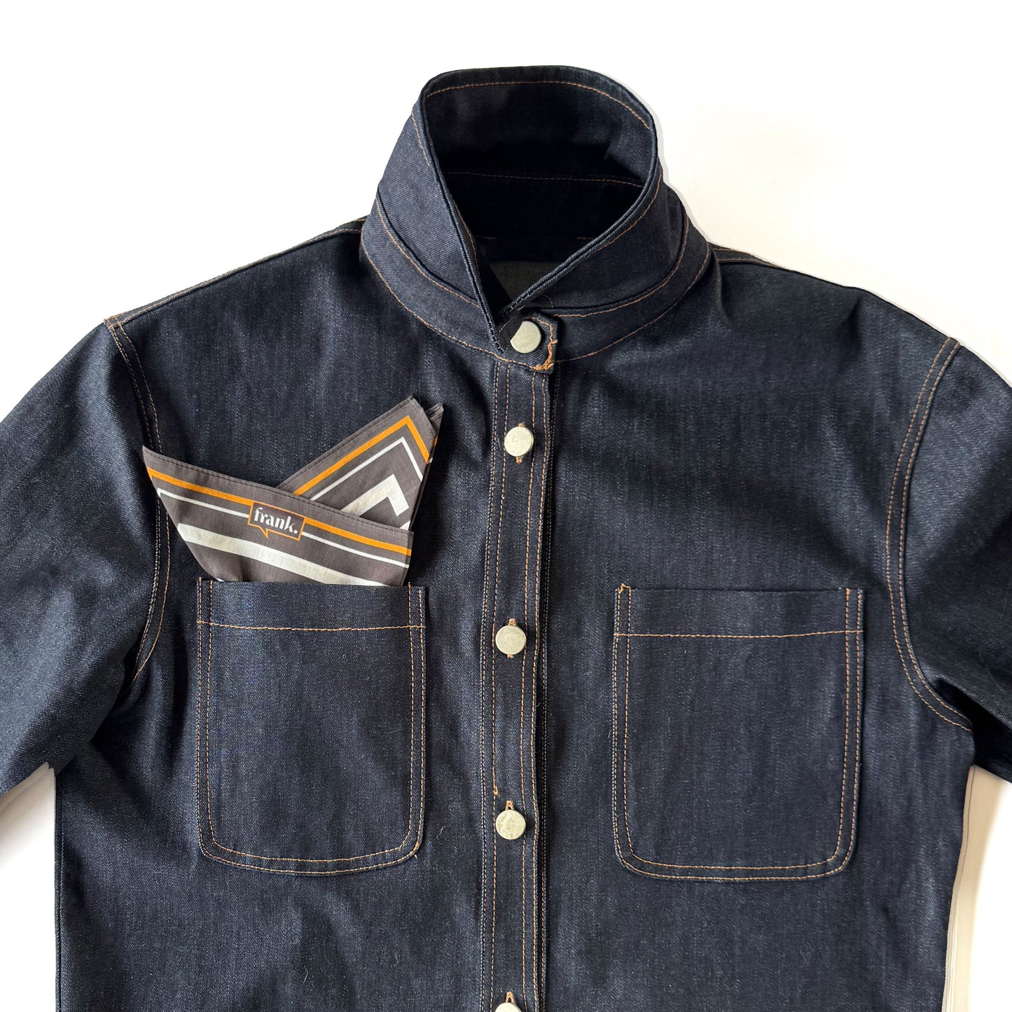 Denim jacket with a black, white and gold striped handkerchief in the pocket on a white background