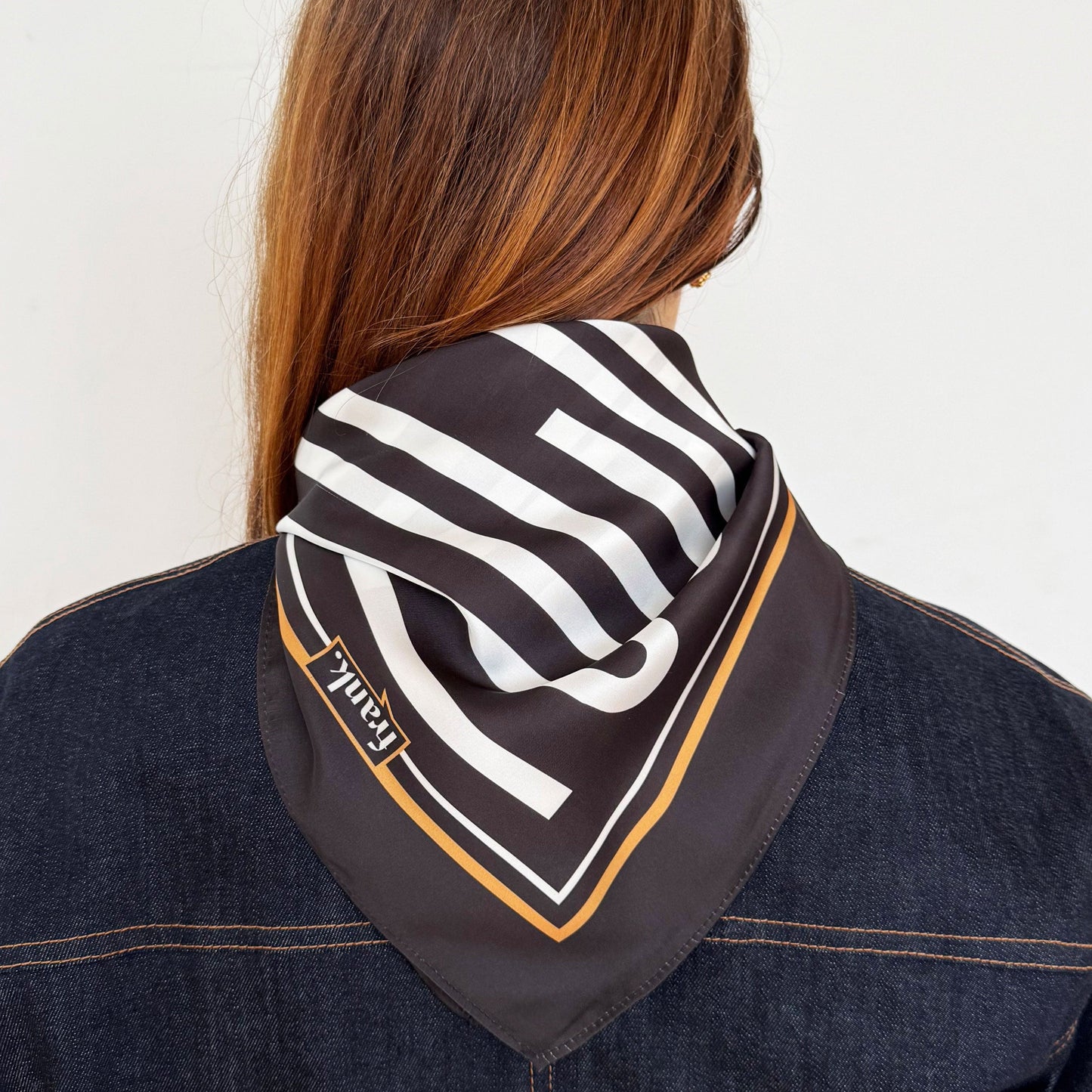 Backview of a person wearing a black and white striped scarf with a brand logo on a plain background