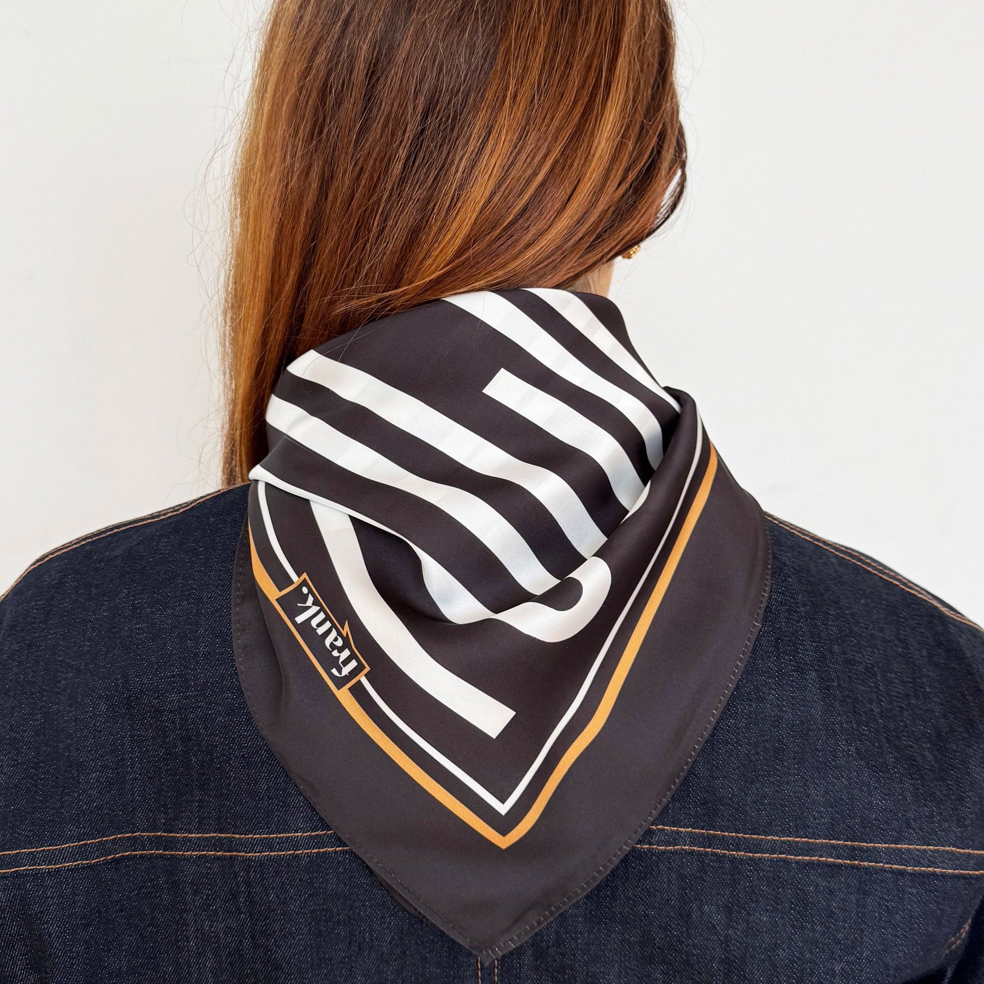 Backview of a person wearing a black and white striped scarf with a brand logo on a plain background