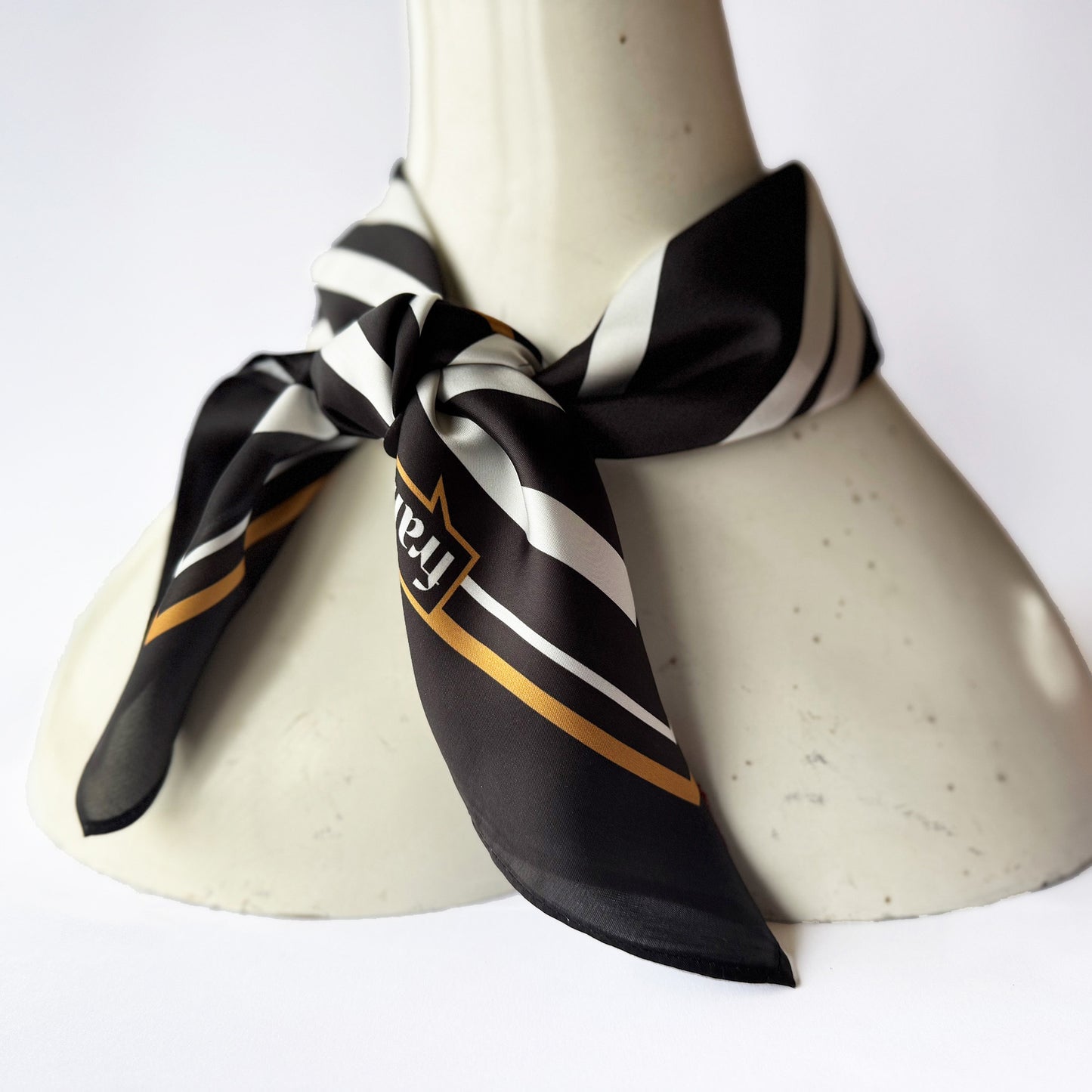Black and white striped scarf with gold accents on a mannequin bust against a white background