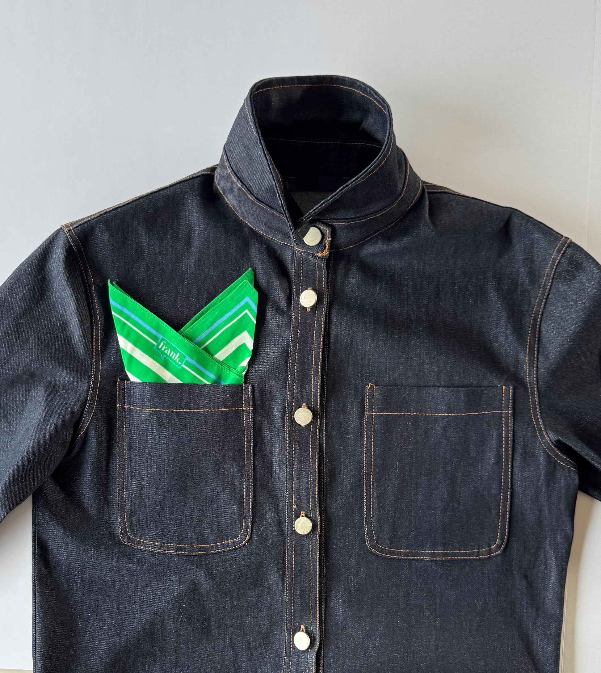Dark denim jacket with a green and white patterned handkerchief in the pocket on a light background