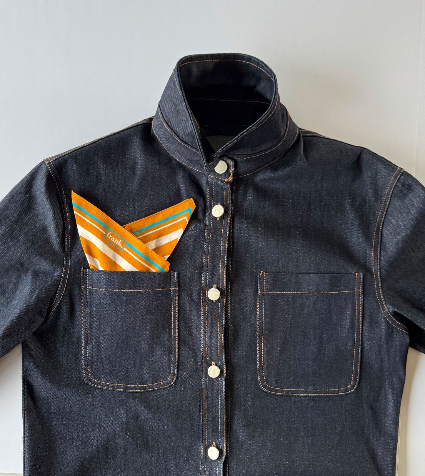 Dark denim jacket with a pocket containing gold striped handkerchief on a light background