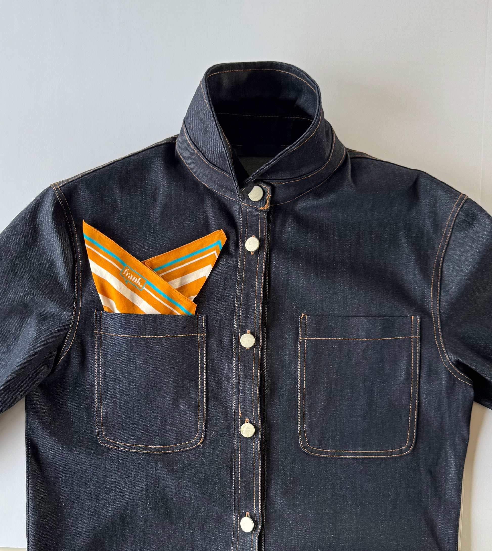 Dark denim jacket with a pocket containing gold striped handkerchief on a light background