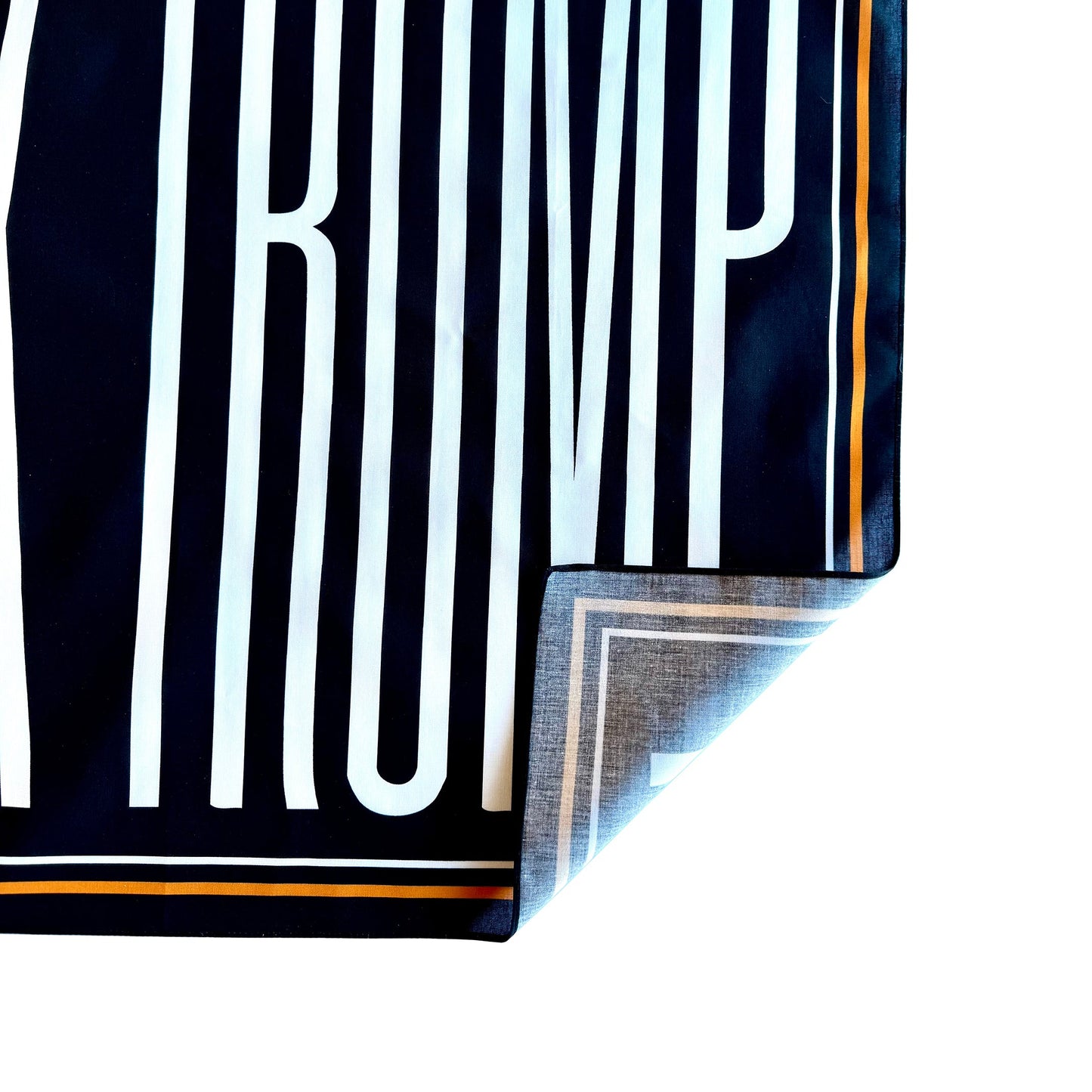 Close-up of a black and white striped fabric with 'TRUMP' printed on it. Corner is turned up to show one-sided printing.