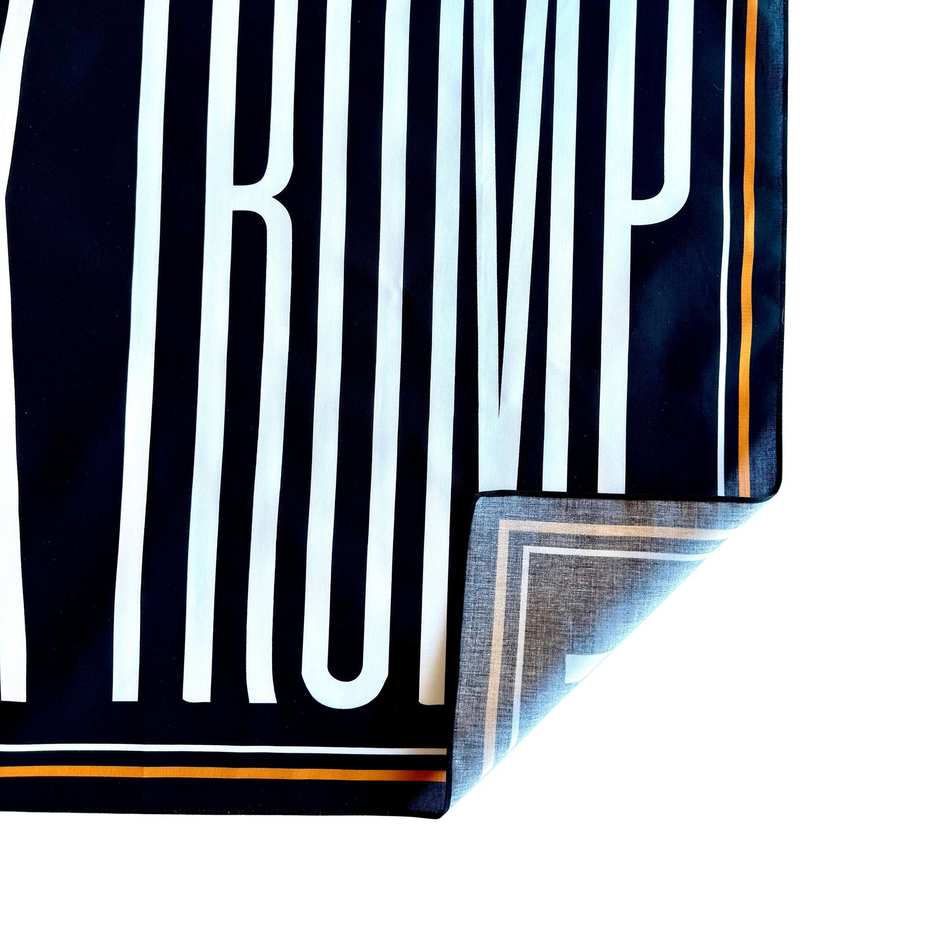 Close-up of a black and white striped fabric with 'TRUMP' printed on it. Corner is turned up to show one-sided printing.