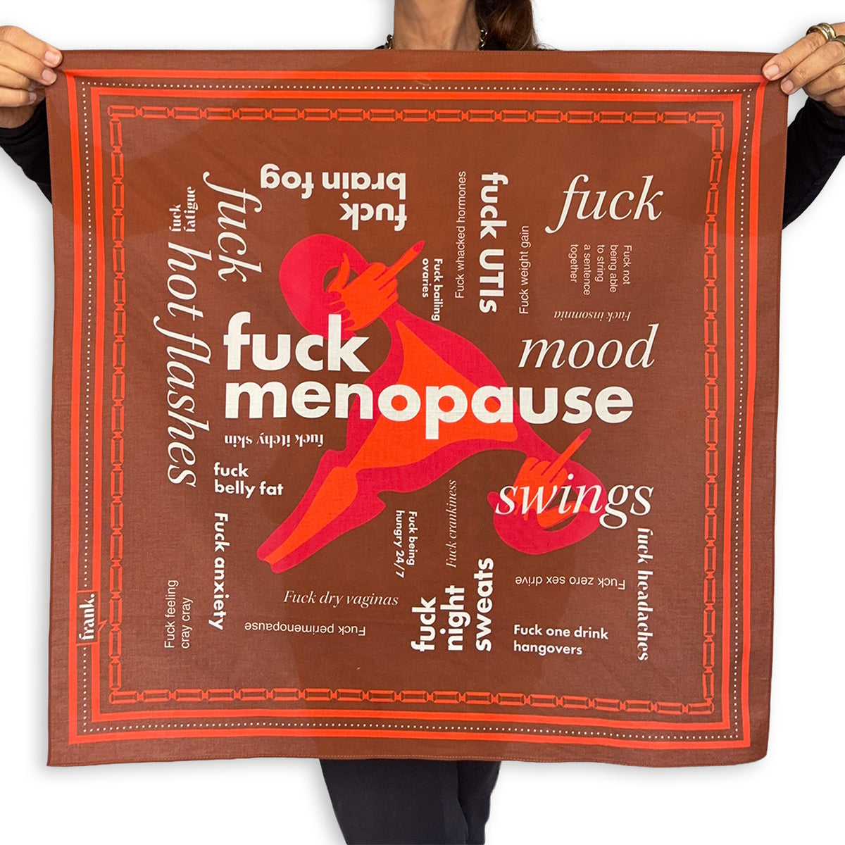 A person holds up a square brown scarf with a bold red and white graphic and text related to menopause and humor, against a plain white background.