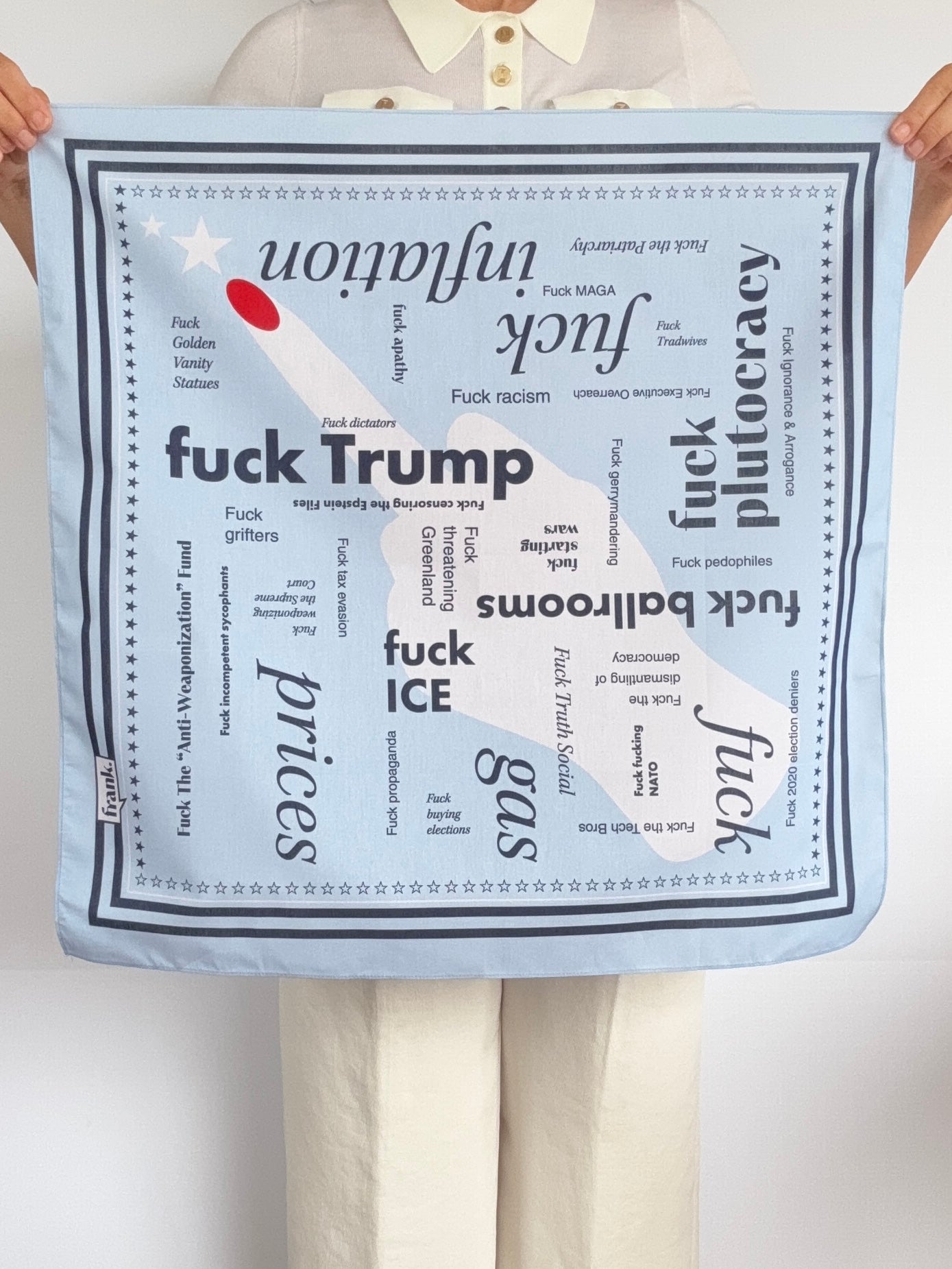 Woman holding a light blue bandana with words in navy blue typography about politics. There is a huge middle finger with red fingernail in the center. Around the border are navy stripes and stars.