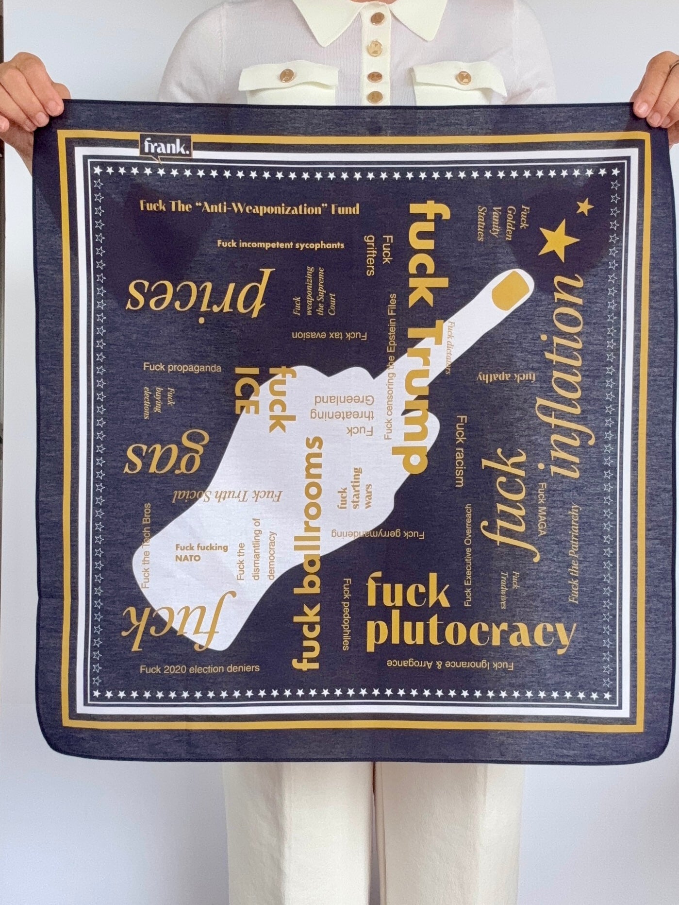 Woman holding a navy blue bandana with words in gold typography about politics. There is a striped border in gold and white stars.