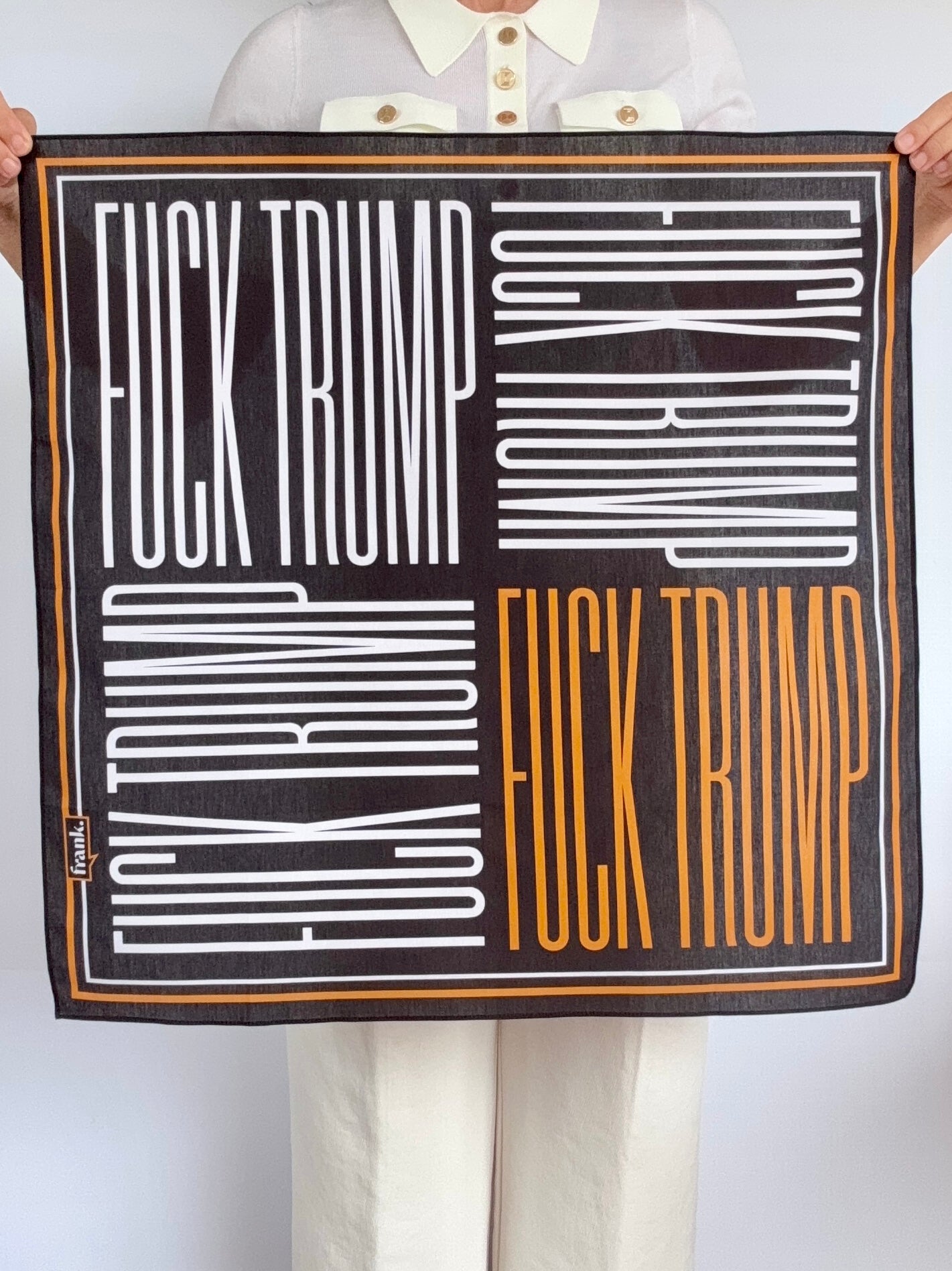 Woman holding black, white, and gold bandana in a quad design, repeating Fck Trump in 4 quadrants.