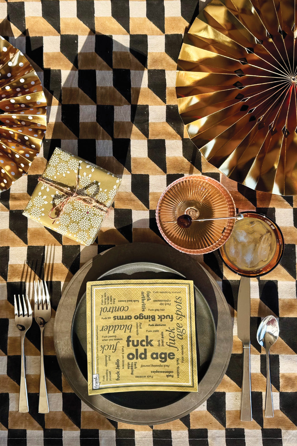 Gold festive table setting with gold Fuck Old napkin on the dinner plate and a swanky cocktail