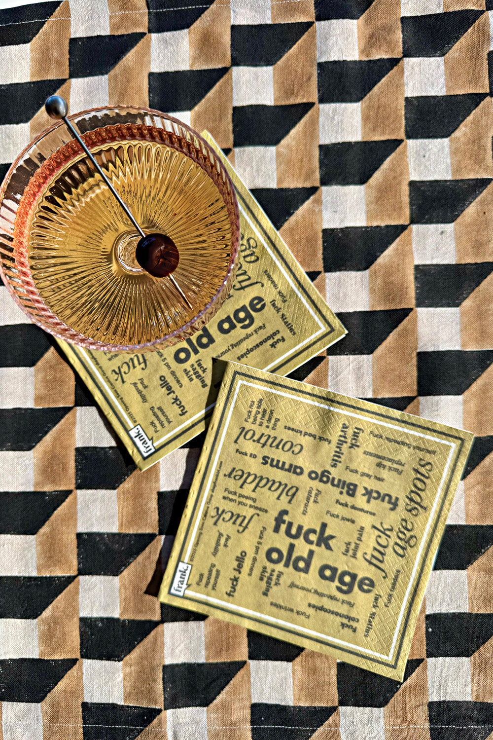 Two gold Fuck Old Age napkins with a swanky cocktail